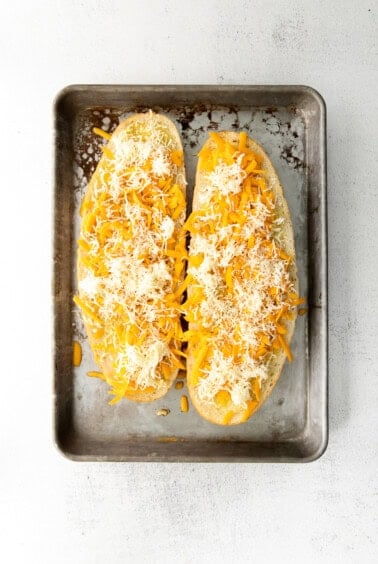 Garlic bread with cheese sprinkled over the top on a baking sheet.