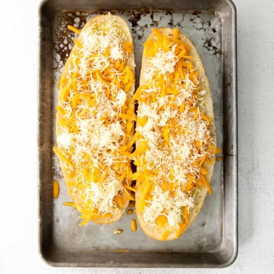 Garlic bread with cheese sprinkled over the top on a baking sheet.