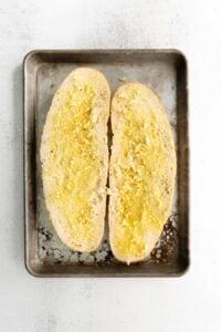 Sliced Italian loaf with butter and garlic spread on both sides.
