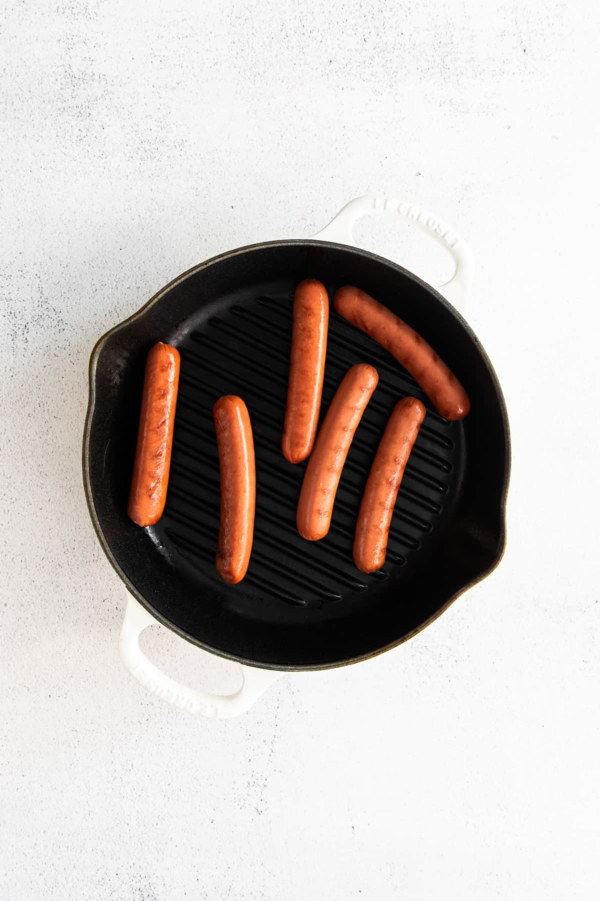 Seared hot dogs in pan.