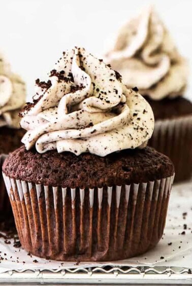 Three chocolate cupcakes topped with whipped cream and powdered sugar.