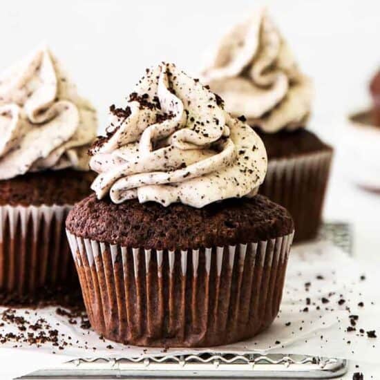 Three chocolate cupcakes topped with whipped cream and powdered sugar.