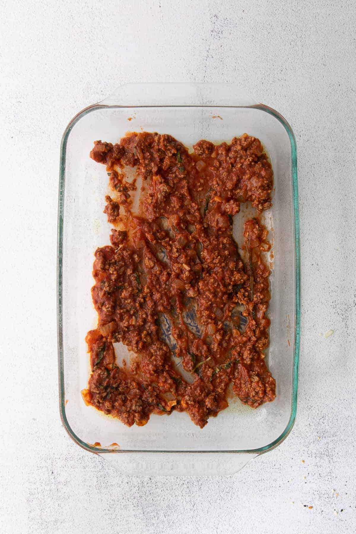 Meat sauce spread in the bottom of a baking dish. 