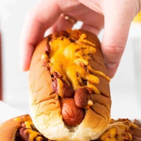 a hand holding a chili cheese dog