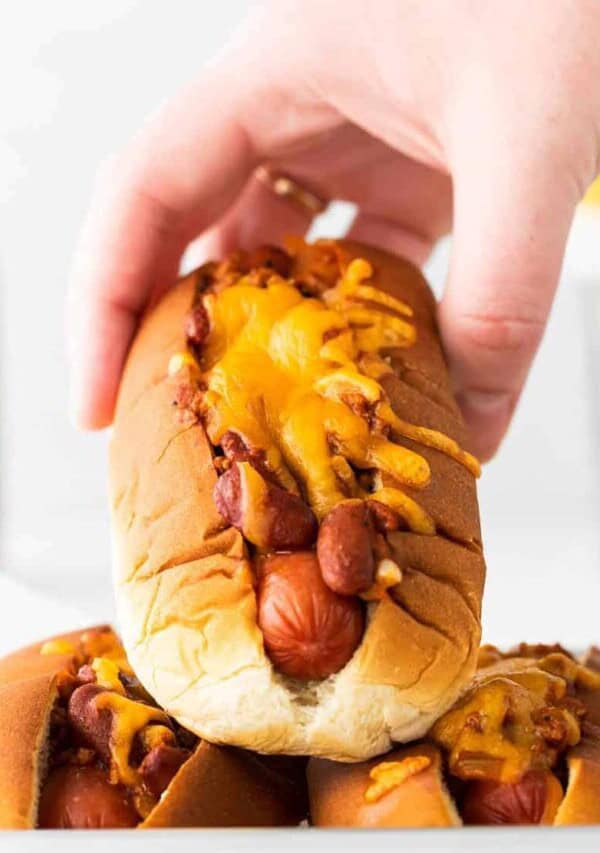 a hand holding a chili cheese dog