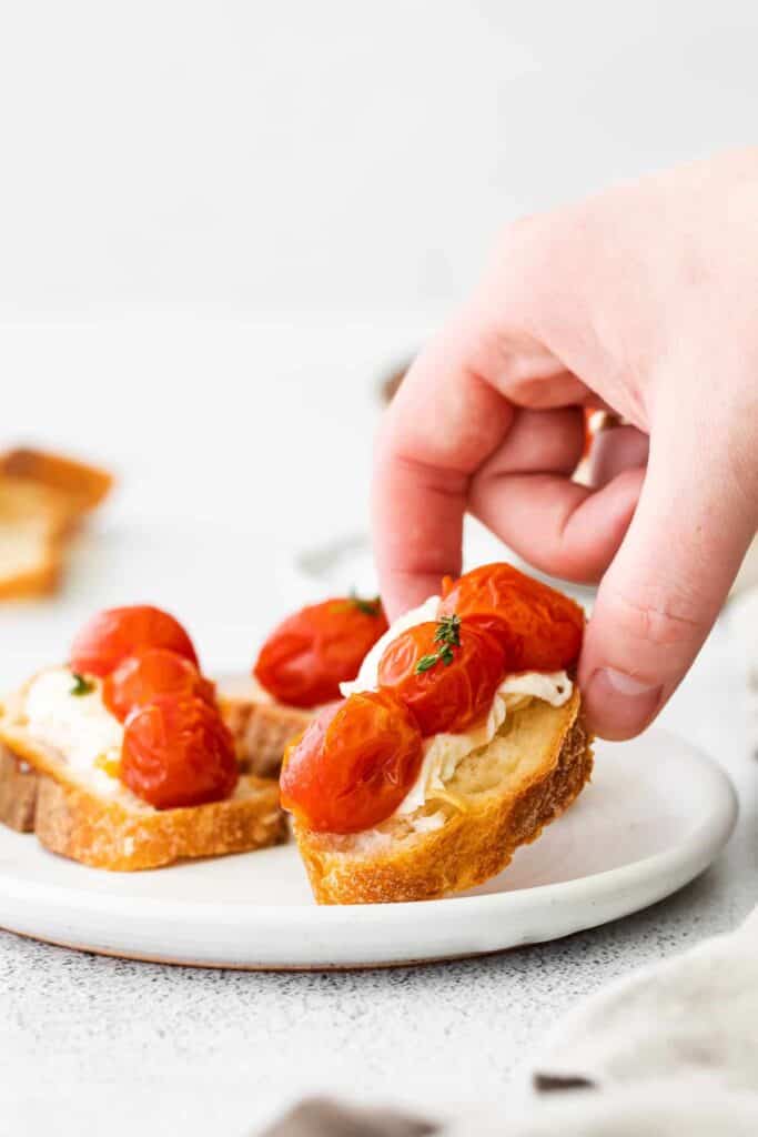 warm burrata and roasted tomatoes on a crostini being picked up by a hand