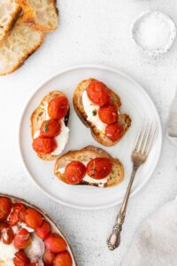 A plate of warm bruschetta topped with roasted tomatoes and burrata cheese.