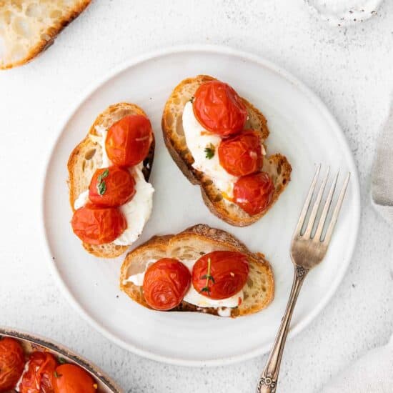 A plate of warm bruschetta topped with roasted tomatoes and burrata cheese.