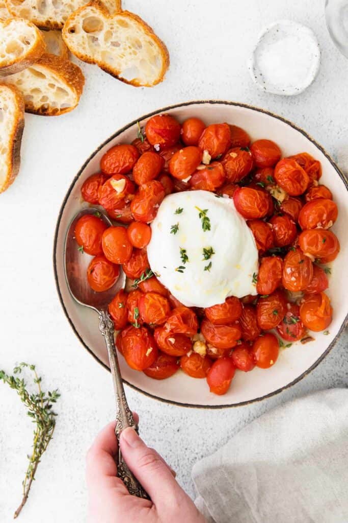 warm burrata and roasted tomatoes in a bowl ready to be served with toasted baguette
