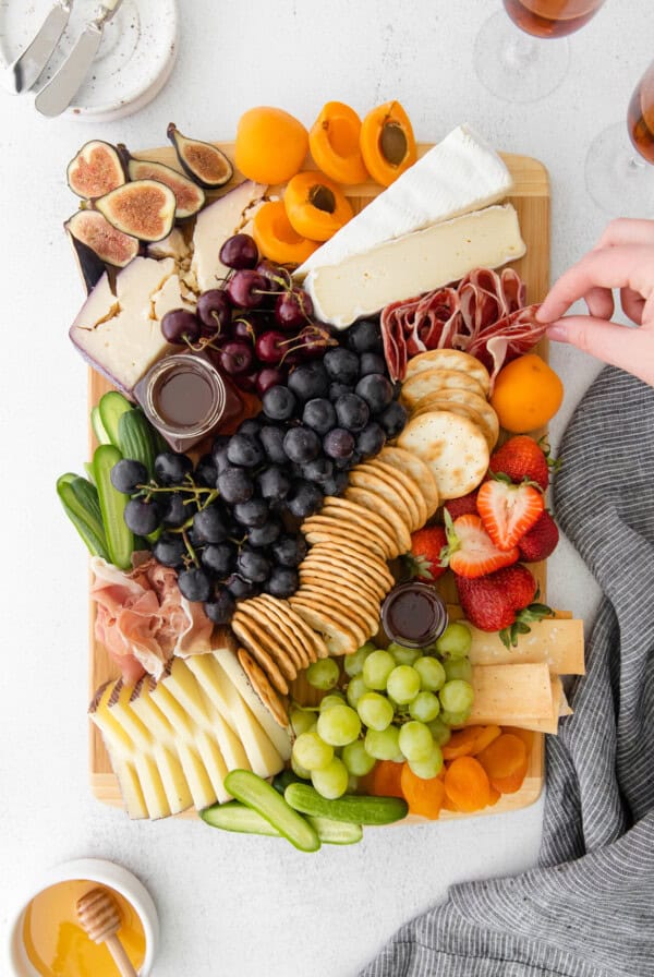 a person is holding a cheese board with fruit, cheese, and crackers.