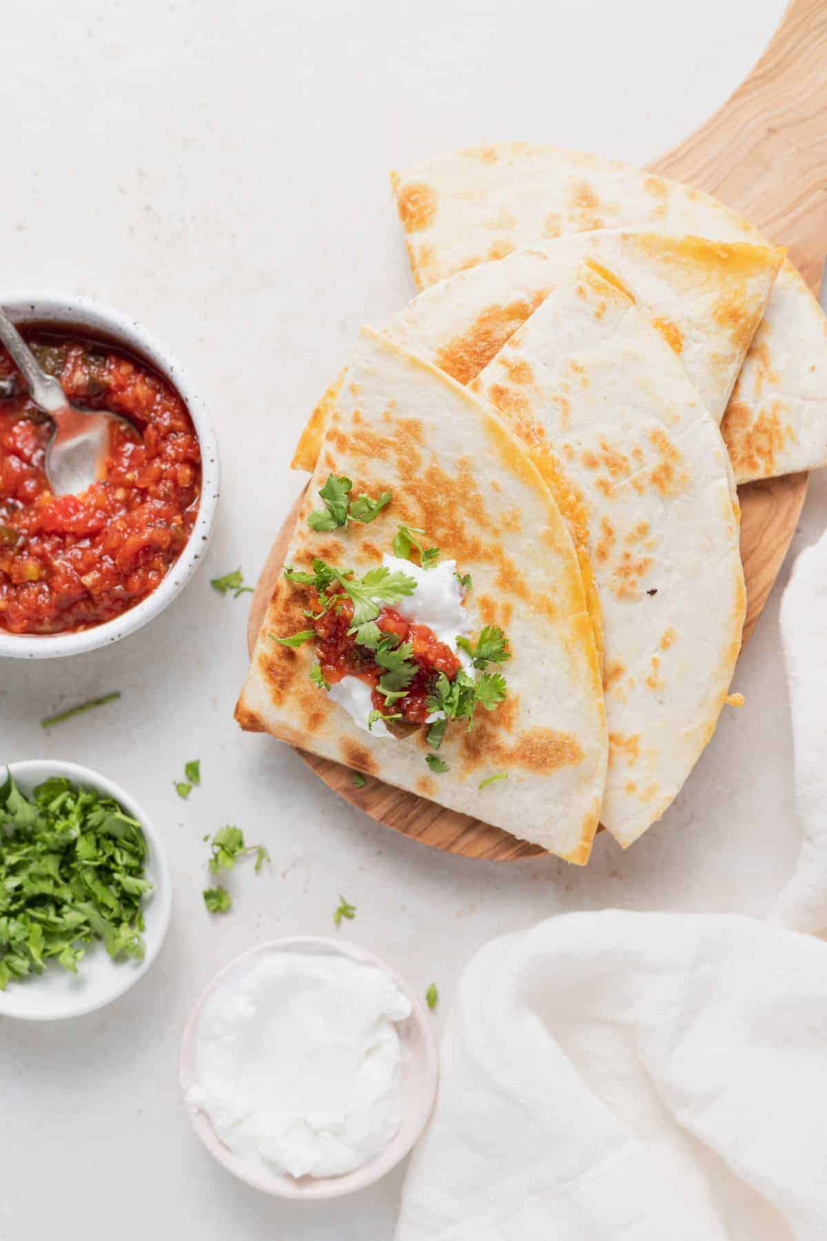 quesadillas on a cutting board with salsa and sour cream.