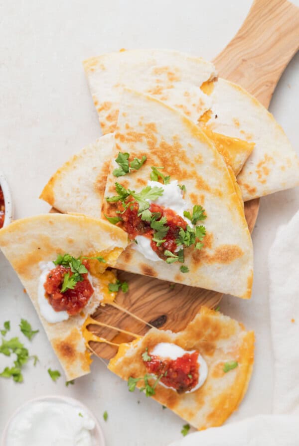 quesadillas on a cutting board with salsa and sour cream.