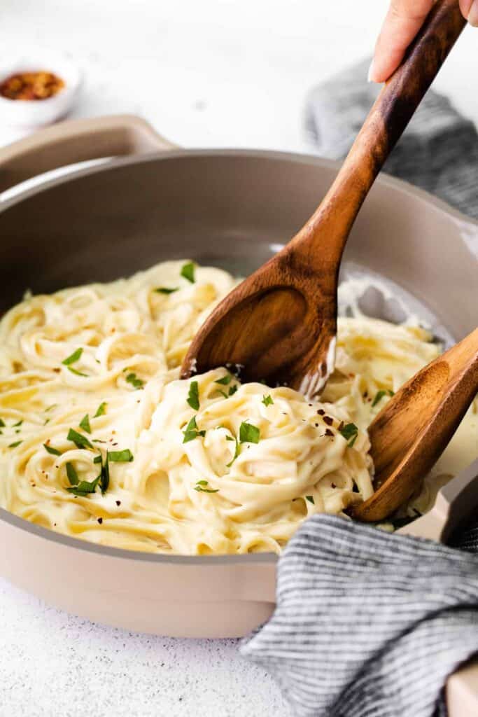 alfredo sauce with cream cheese in a skillet being tossed into fettuccine. 