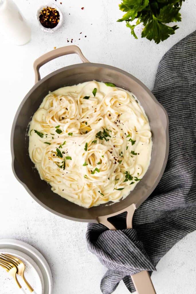 A frying pan of pasta and herbs tossed in alfredo sauce.