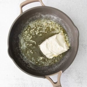 A frying pan with creamy alfredo sauce and a piece of cheese.