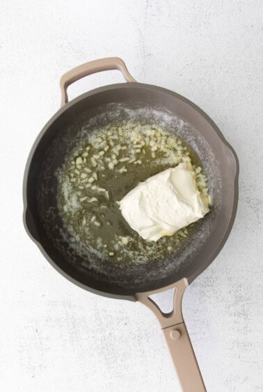 A frying pan with creamy alfredo sauce and a piece of cheese.