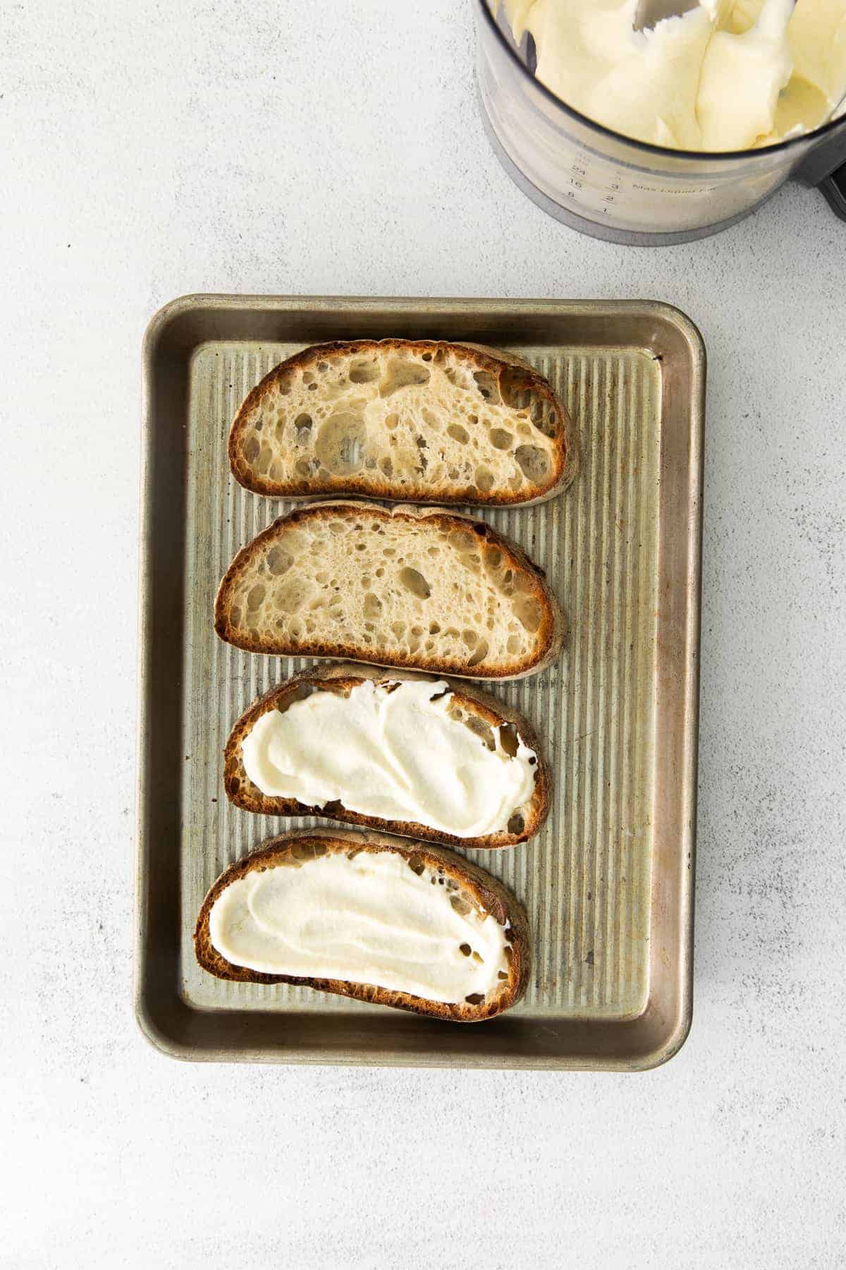 Ricotta toast on a baking sheet topped with ricotta cheese. 