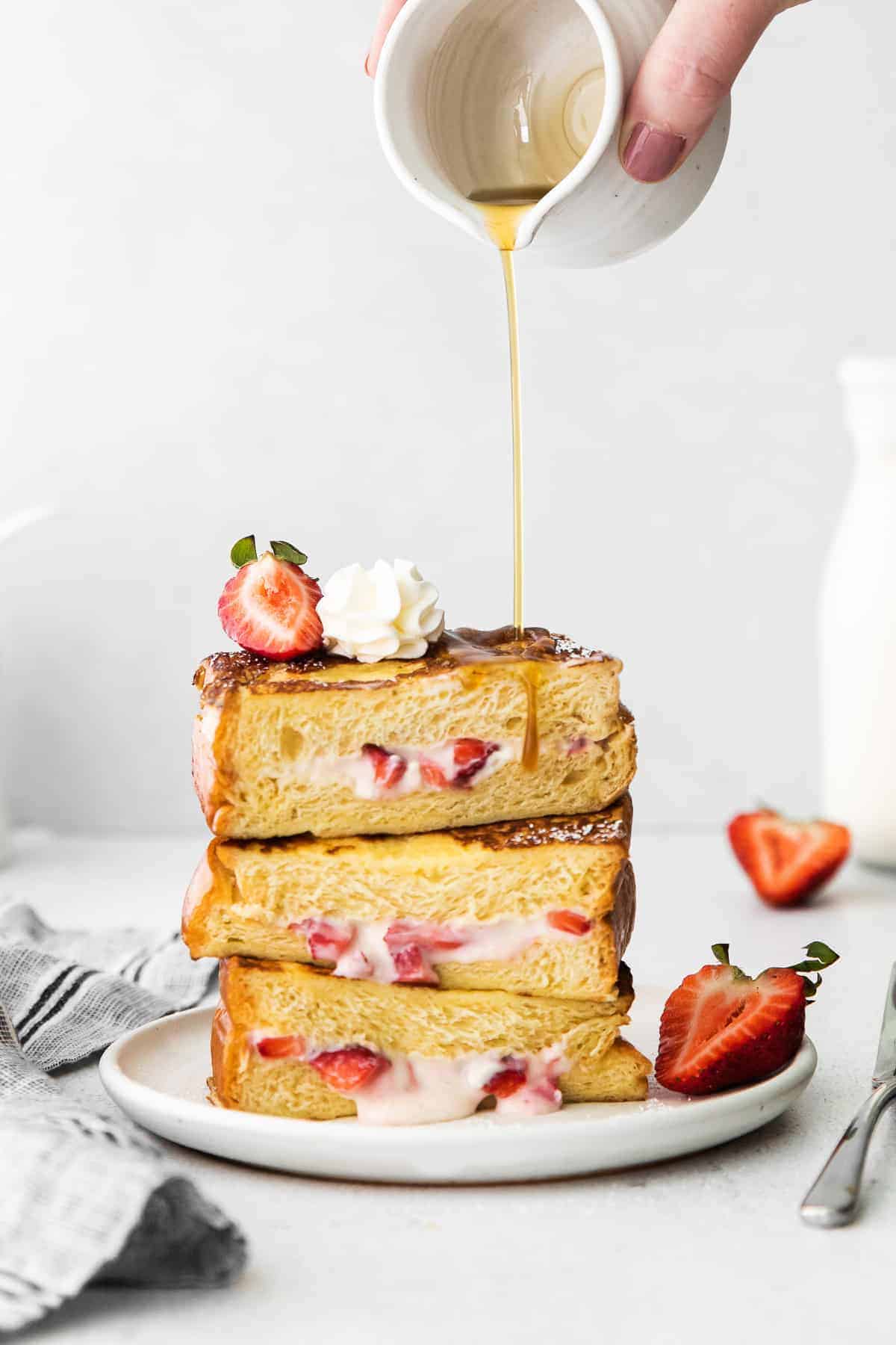 Stuffed french toast with maple syrup being poured over it.