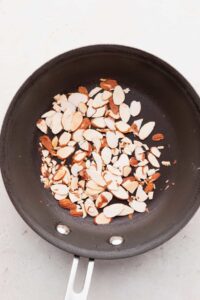 A frying pan with almonds used in an arugula goat cheese salad.