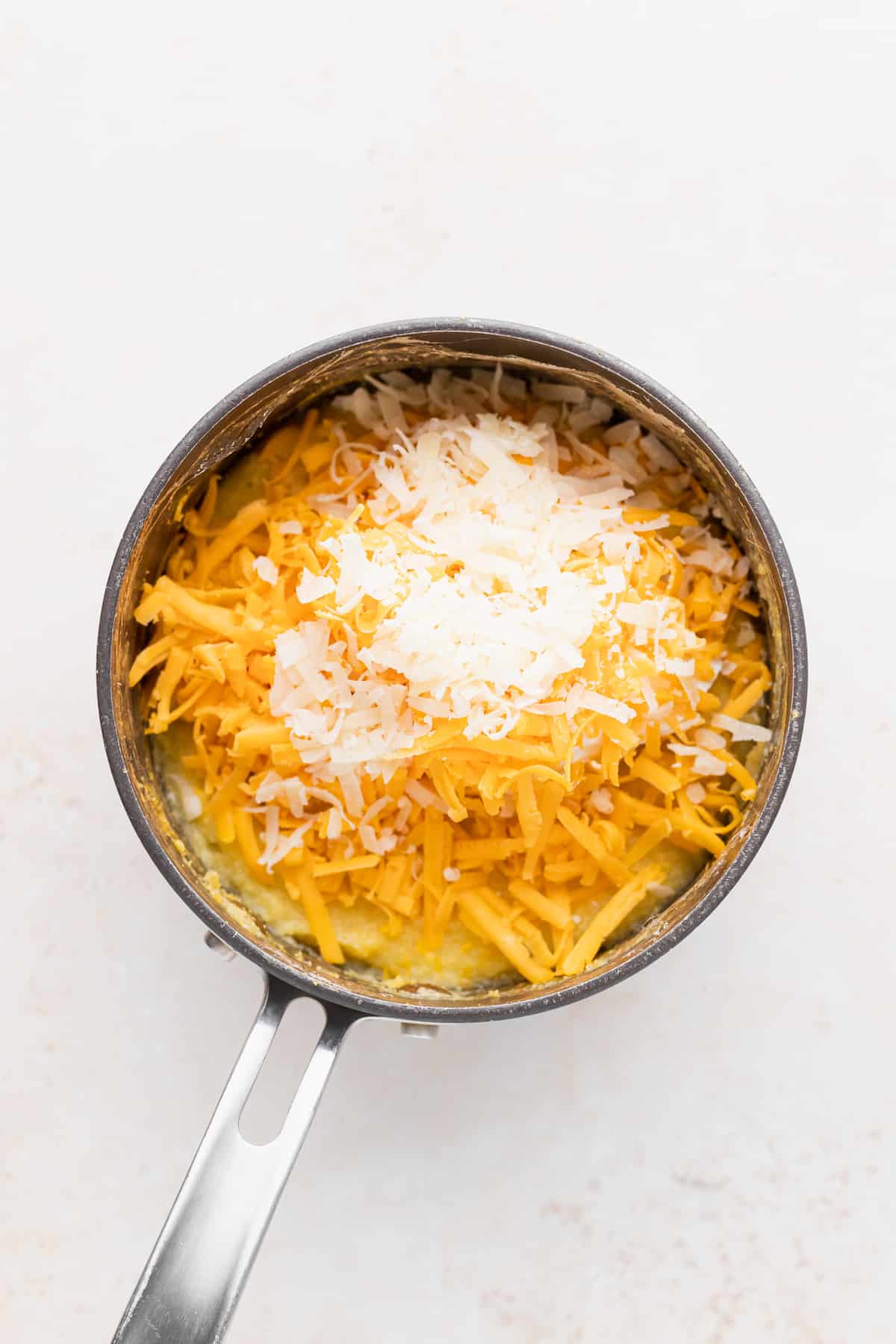 shredded parmesan cheese and yellow cheddar cheese in a pot with grits