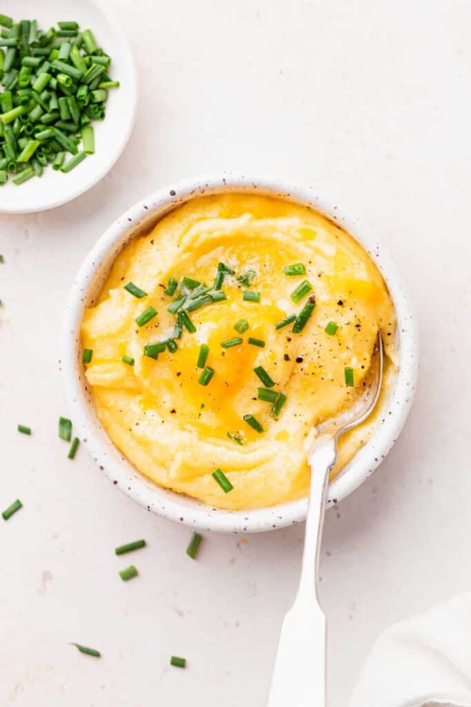 cheese grits in a bowl with a spoon topped with fresh chives 