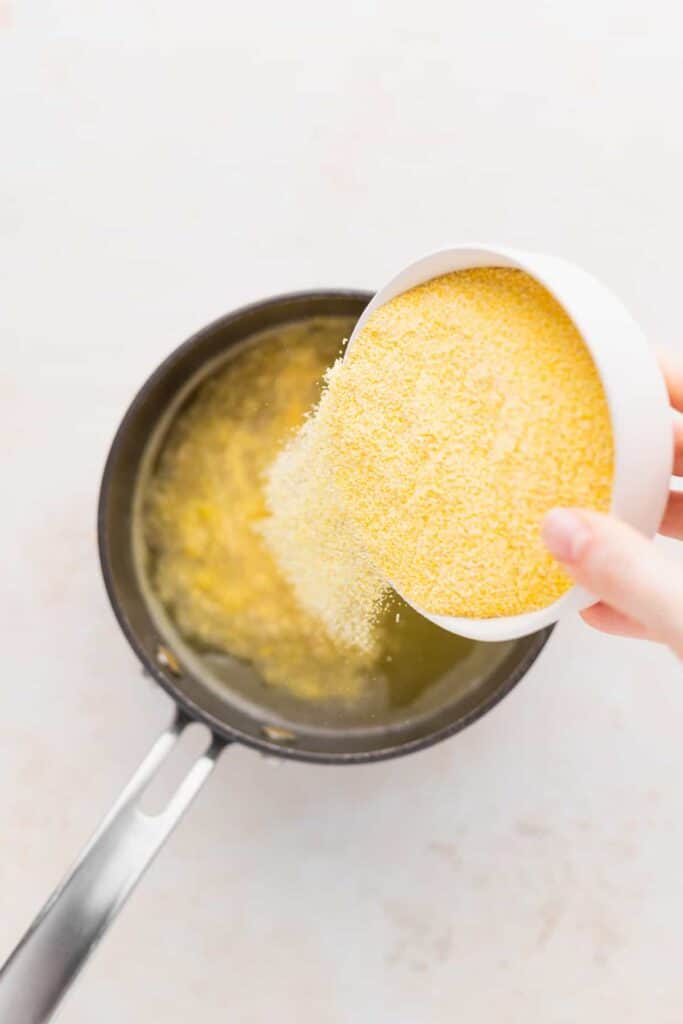 cornmeal being poured into broth for cheese grits