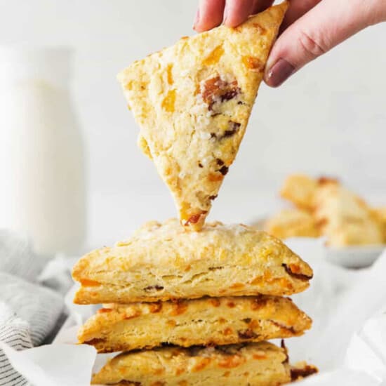 a person grabbing a slice of scones from a baking sheet.