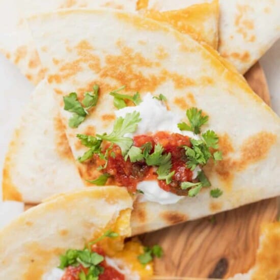 closeup image of a cheese quesadilla topped with greek yogurt, salsa and cilantro