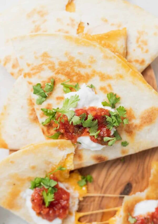 closeup image of a cheese quesadilla topped with greek yogurt, salsa and cilantro