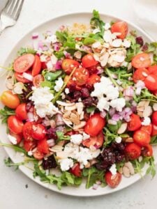 a plate of cranberry arugula salad with feta and almonds.