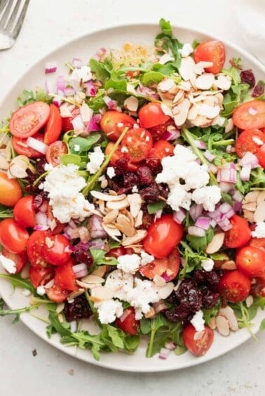 a plate of cranberry arugula salad with feta and almonds.