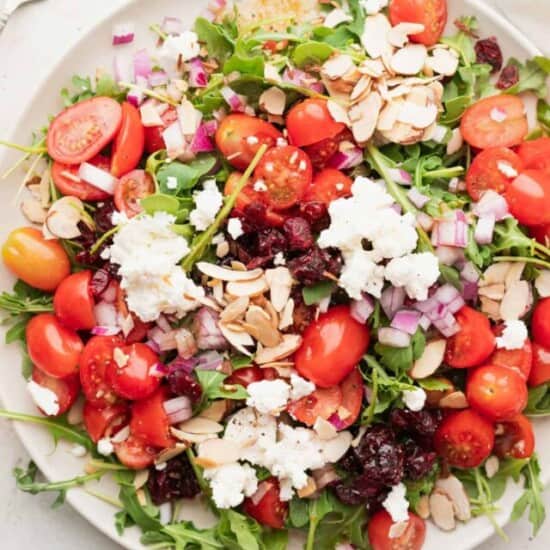 a plate of cranberry arugula salad with feta and almonds.