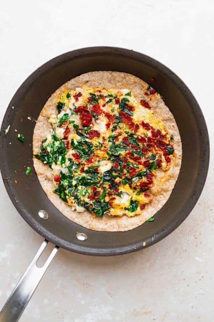 A tortilla topped with eggs, spinach, and sun dried tomatoes. 