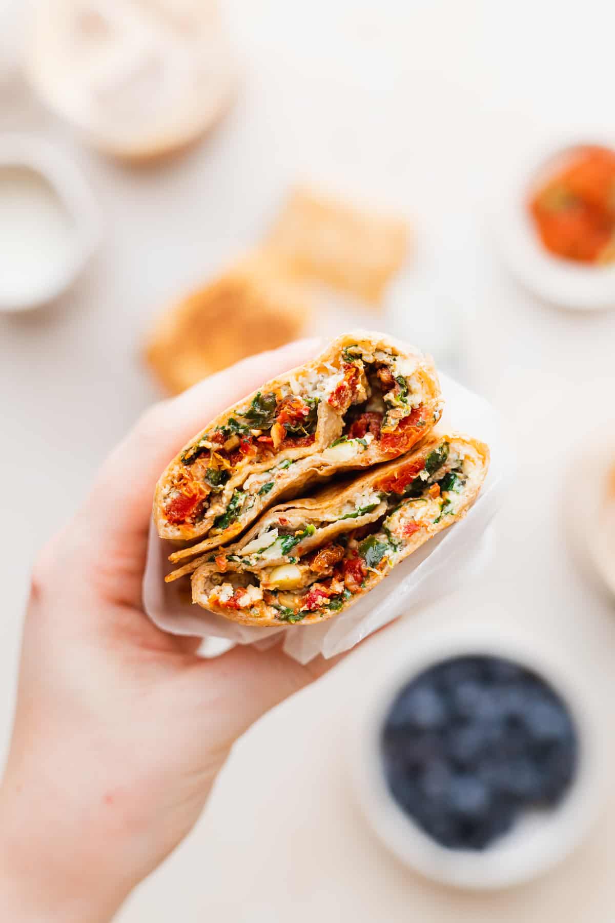 A hand holding a spinach feta wrap that is wrapped in wax paper. 