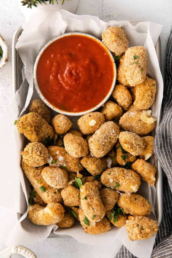 air fryer cheese curds in a basket with a bowl of marinara sauce