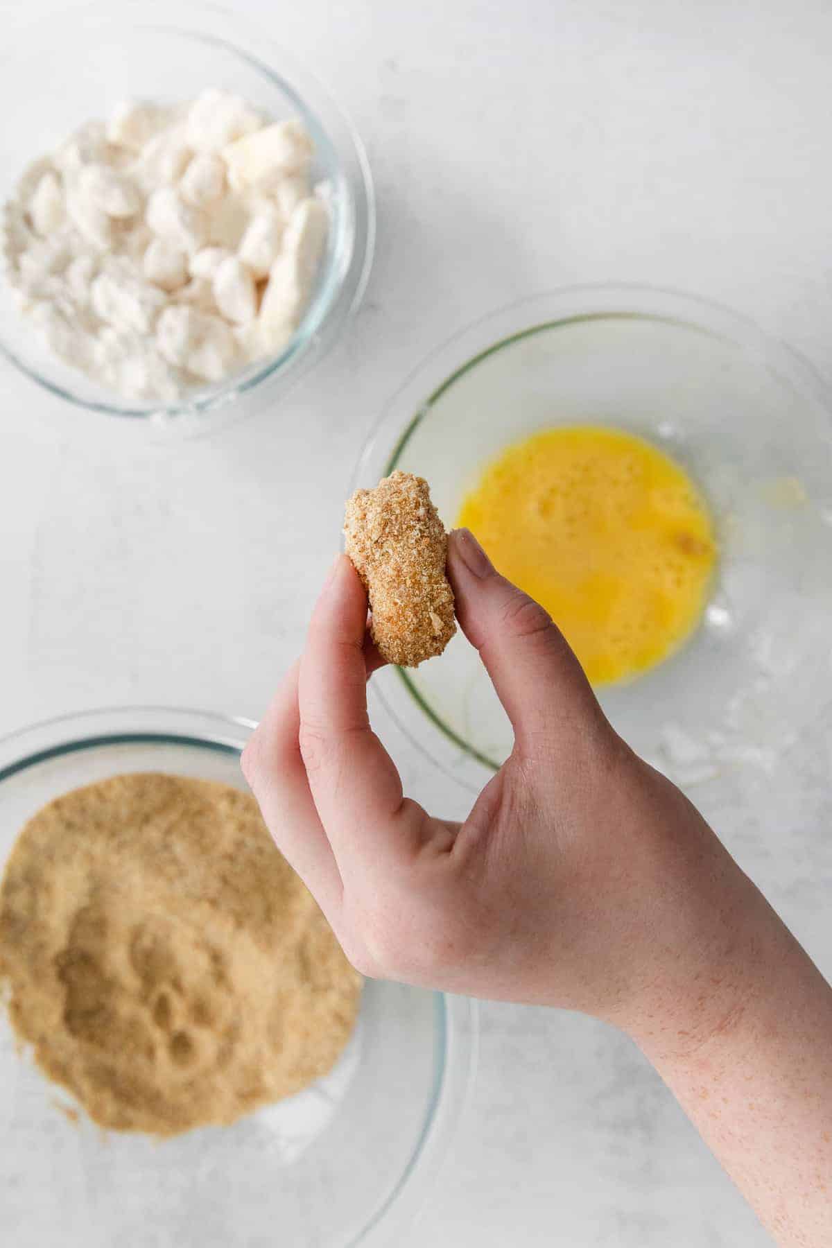 cheese curd with breading about to be dipped into an egg wash