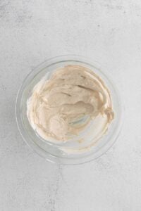 Whipped cream and cream cheese in a glass bowl on a white surface.