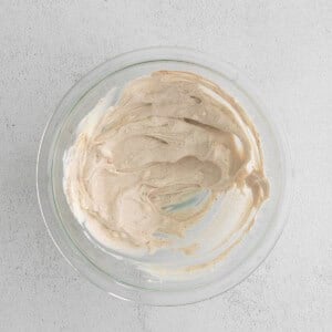 Whipped cream and cream cheese in a glass bowl on a white surface.