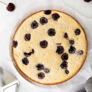 A cherry ricotta cake served on a plate with a knife nearby.