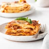 Meat lasagna on a plate with fresh basil on top.