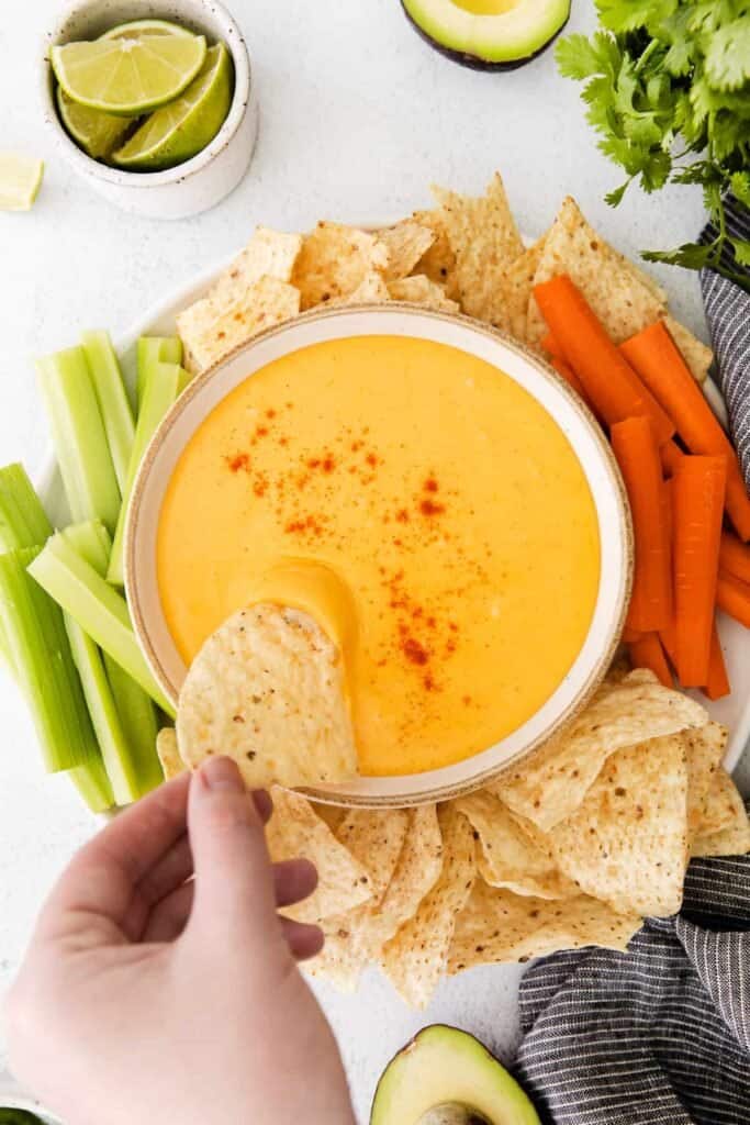 Nacho Cheese Sauce surrounded by chips, carrots, and celery. 