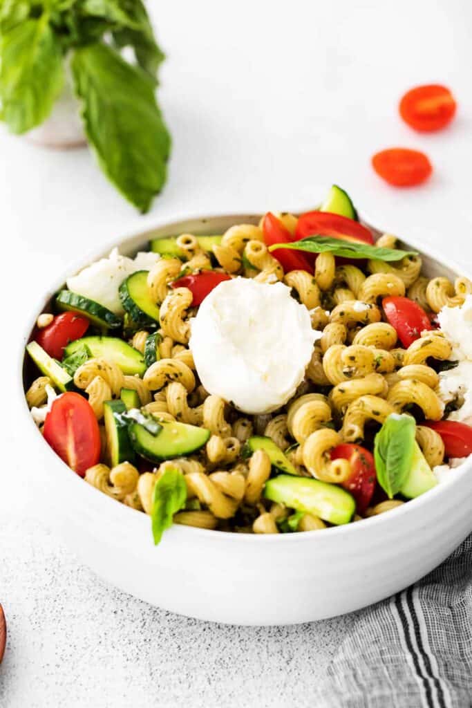 a ball of burrata pulled apart into chunks and placed over pesto pasta salad