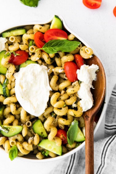 A flavorful bowl of pesto pasta salad with tomatoes, cucumbers, and feta cheese.