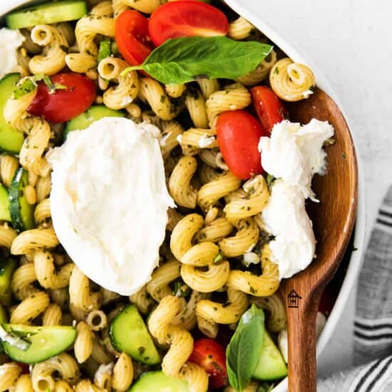 A flavorful bowl of pesto pasta salad with tomatoes, cucumbers, and feta cheese.