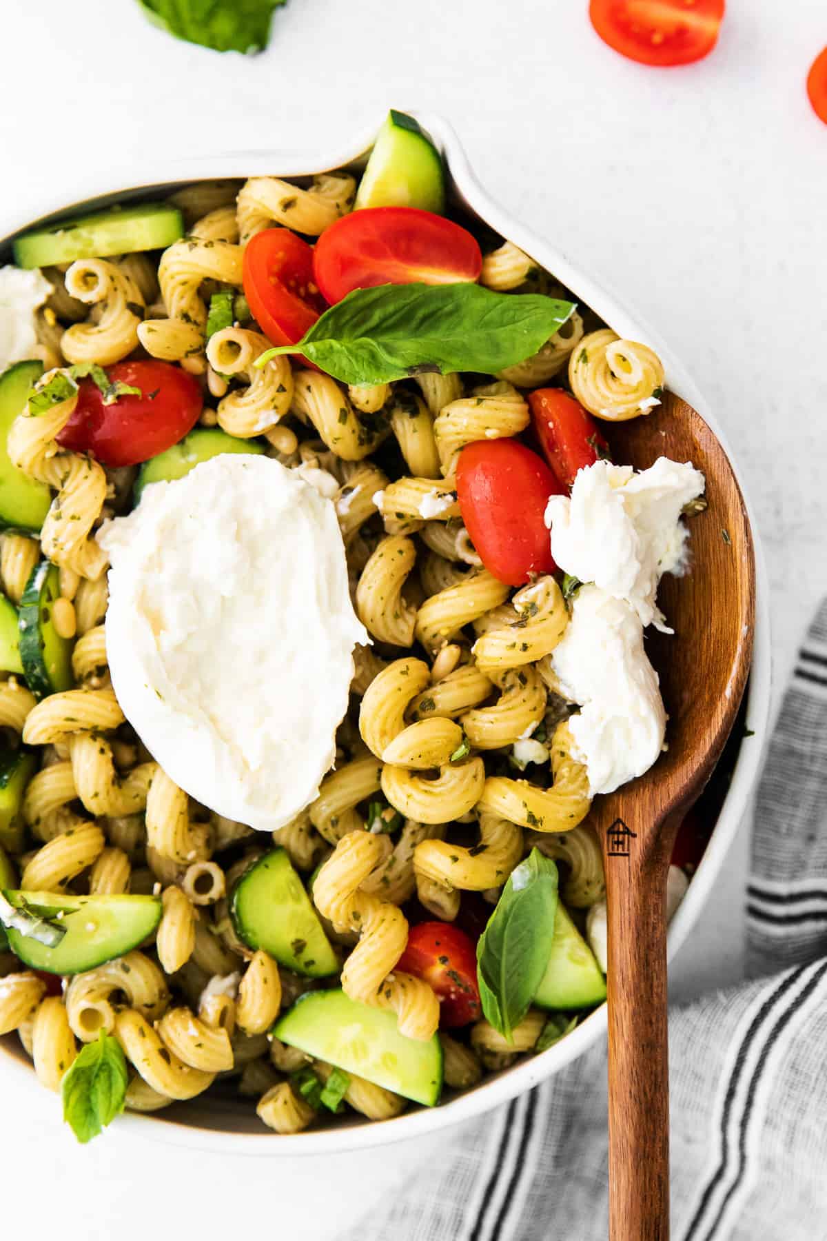 pesto pasta salad with burrata in a bowl with a wooden spoon ready to serve a delicious scoop