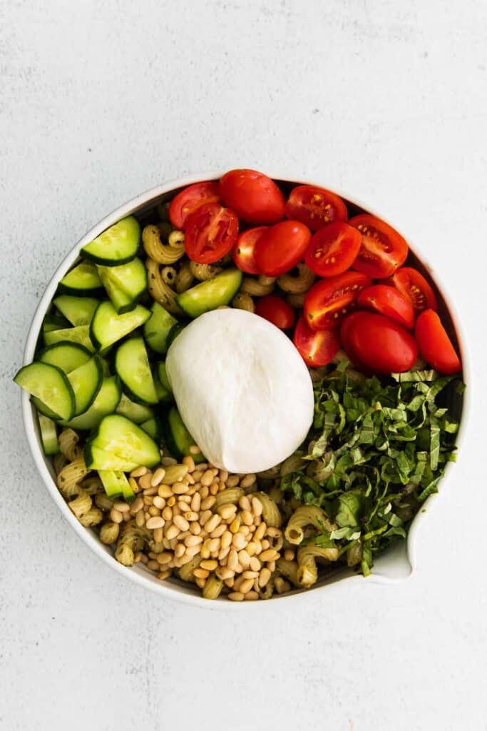 pesto pasta salad ingredients in a bowl and topped with a ball of burrata