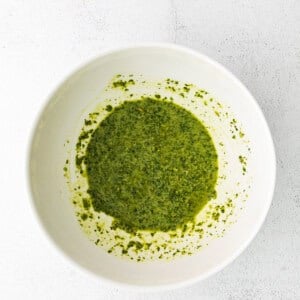 A bowl of green pesto with burrata on a white surface.