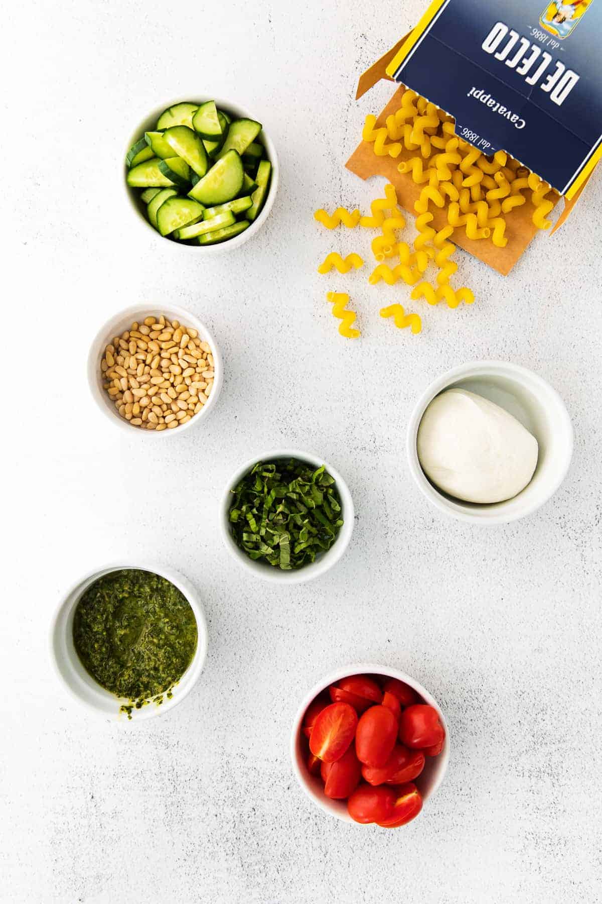 Pesto pasta salad ingredients in bowls.