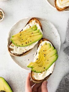 avocado toast on a plate with a hand holding it.