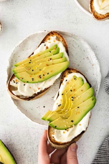 avocado toast on a plate with a hand holding it.
